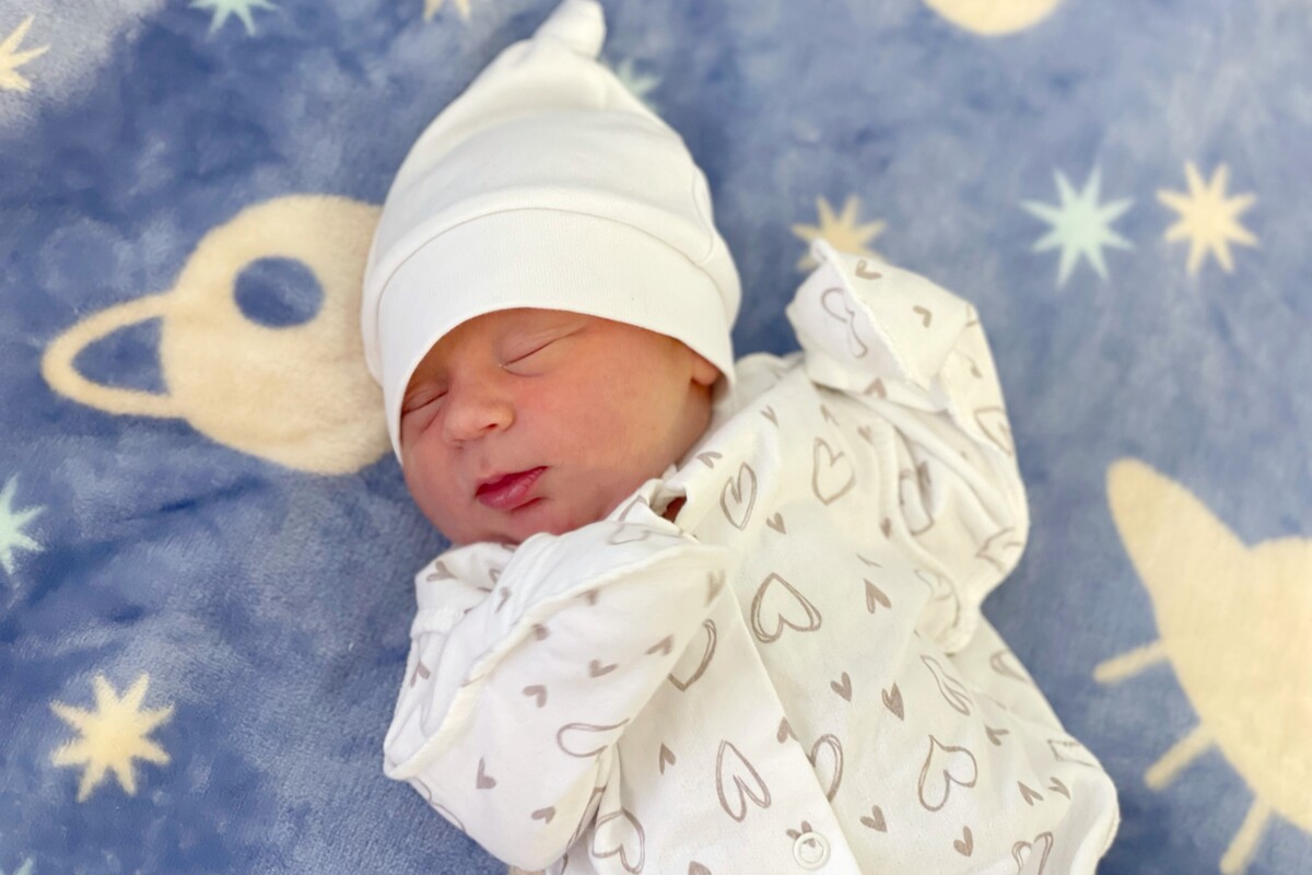 На синій постелі із зірочками спить Матвійко; він одягнений у білу шапочку та сорочечку із сердечками